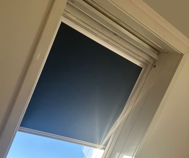 Thermo Dachfensterrollo im Dachgeschoss, zum Hitzeschutz und zur Lichtregulierung - mit Seitenschienen um Lichteinfall zu vermeiden.